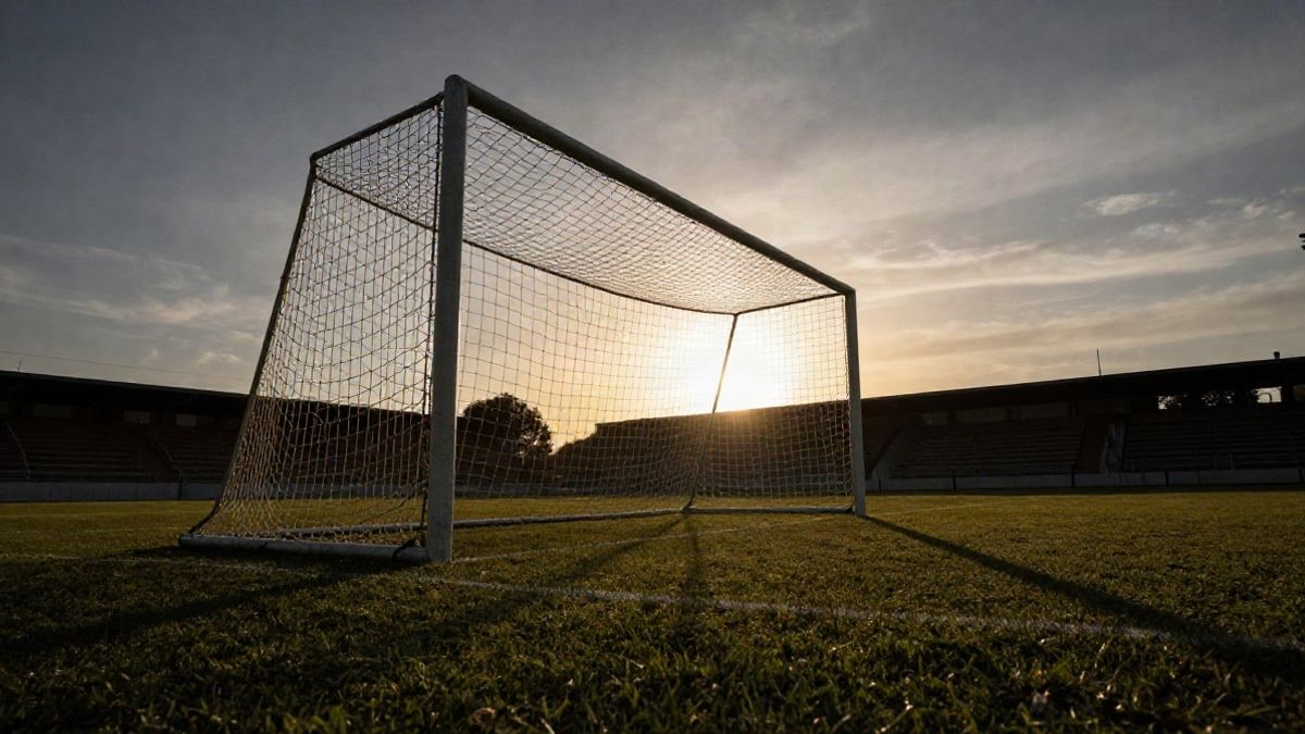 Imagen ilustrativa: portería de fútbol con la red a contraluz al atardecer y sombras largas sobre el césped