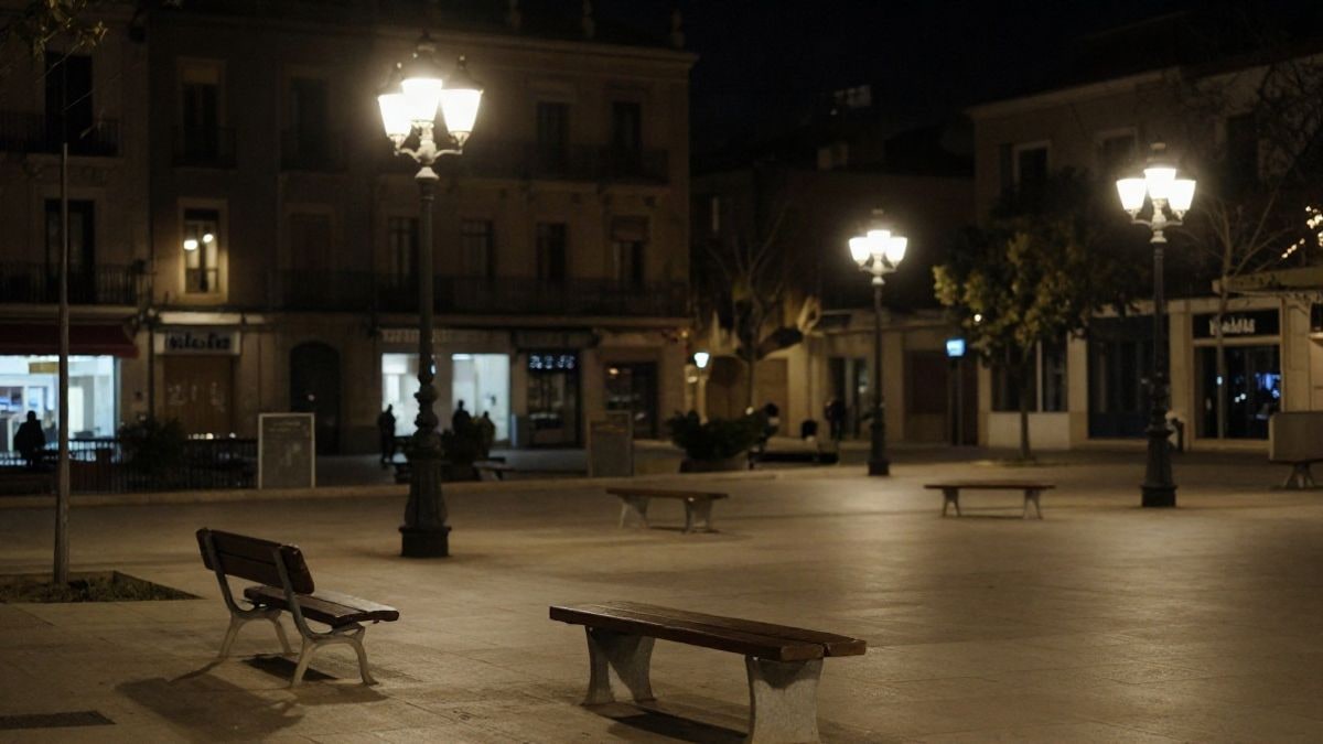 Imagen ilustrativa: plaza urbana nocturna con bancos vacíos y luz artificial tenue