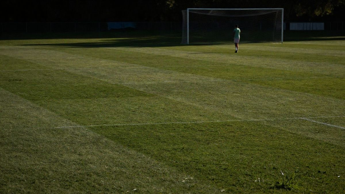 Imagen ilustrativa: un campo de fútbol vacío al atardecer con un jugador solitario de espaldas en la distancia