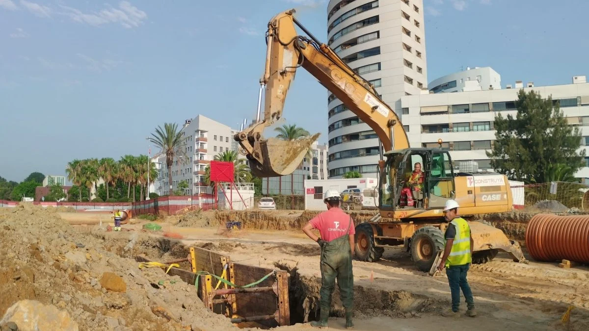 Imagen ilustrativa: vista cenital de una obra de urbanización con zanjas y tuberías en una zona residencial al atardecer.