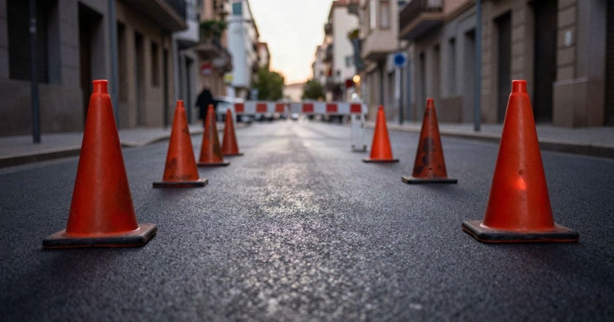 Imagen ilustrativa: avenida urbana cortada al tráfico con conos y una barrera provisional al atardecer