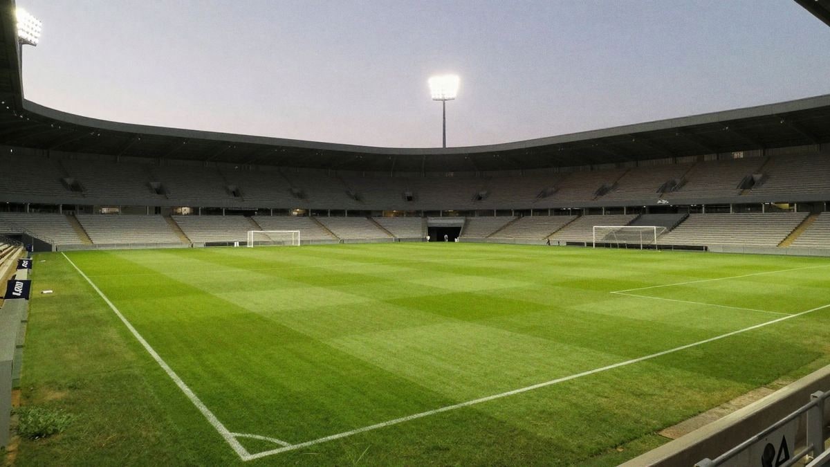 Estadio de fútbol al atardecer, con el campo iluminado y gradas vacías, listo para el partido.