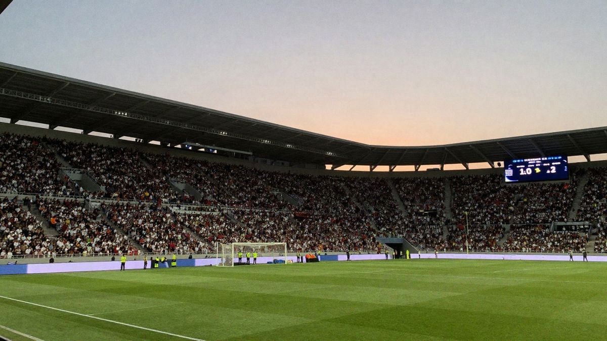 (Generado con IA) Estadio de fútbol al atardecer, con una multitud animada y un campo de juego en primer plano.