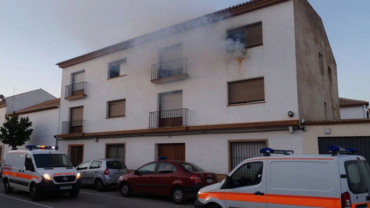 Un bloque de pisos en Isla Cristina envuelto en humo, con vehículos de emergencia en la escena durante la tarde.